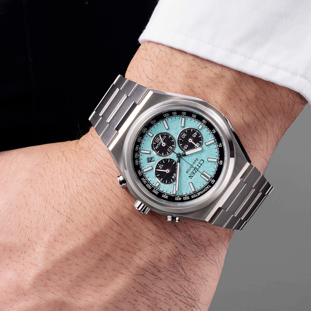 Citizen silver watch with a turquoise face on a wrist against a neutral background