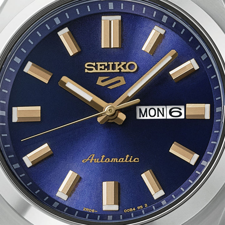 Seiko 5 Sports SRE021K1 dial close-up — deep navy blue sunburst finish, gold baton hour markers, gold dauphine hands, and day-date display at 3 o&