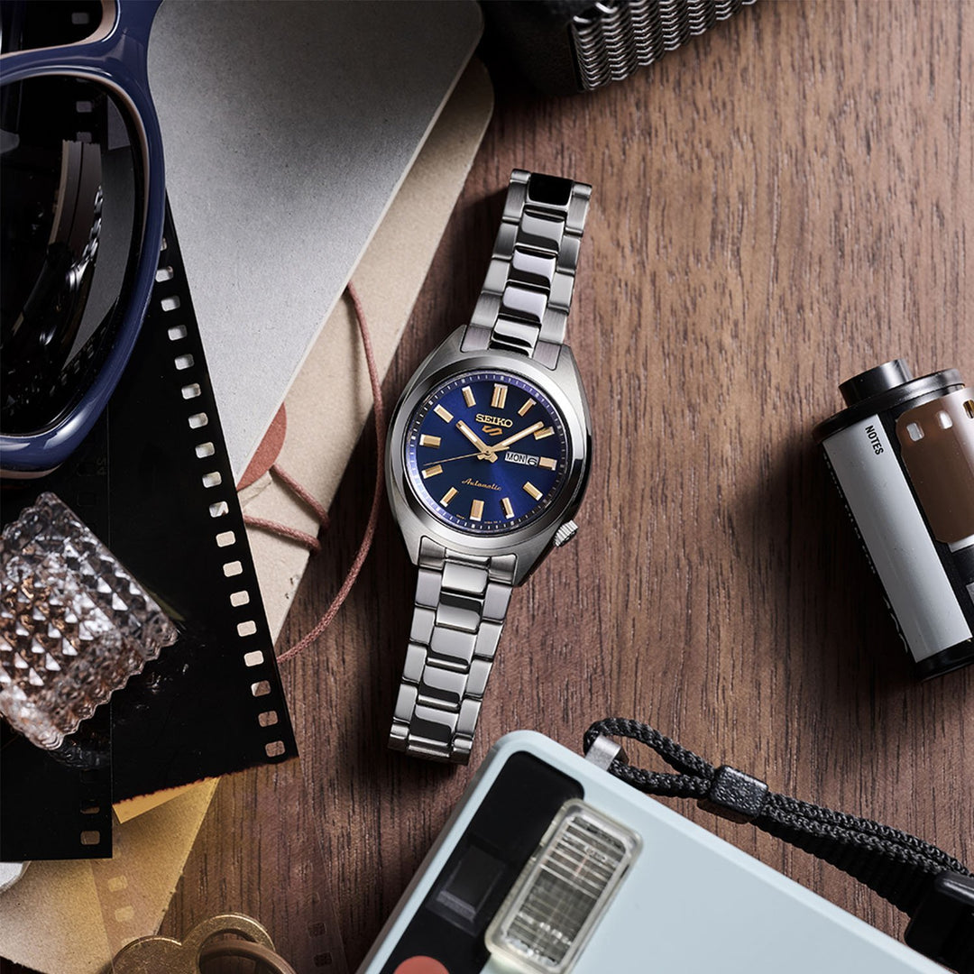 Seiko 5 Sports SRE021K1 navy dial watch in flatlay on a wooden surface, surrounded by film strips, sunglasses, a camera and vintage accessories