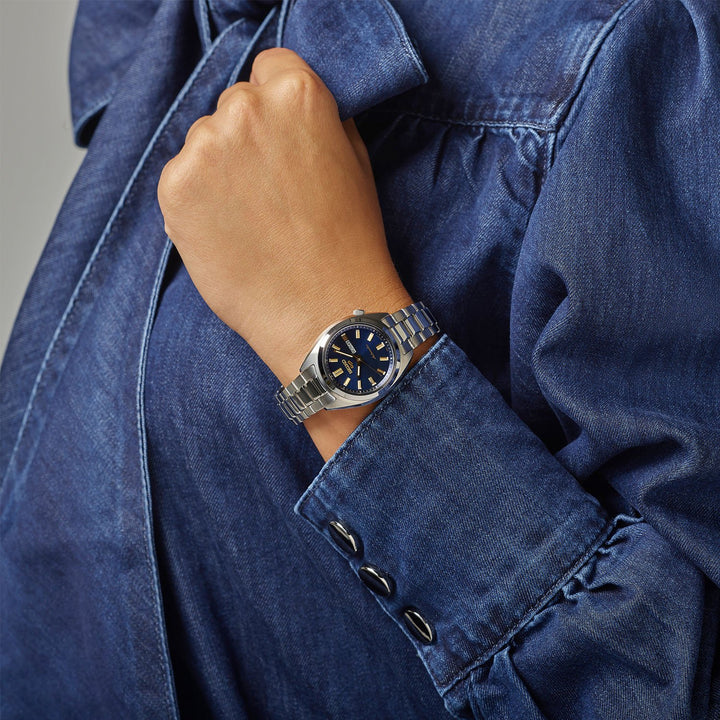 Seiko 5 Sports SRE021K1 navy dial automatic watch worn on wrist, styled with a denim shirt, hand raised to chest
