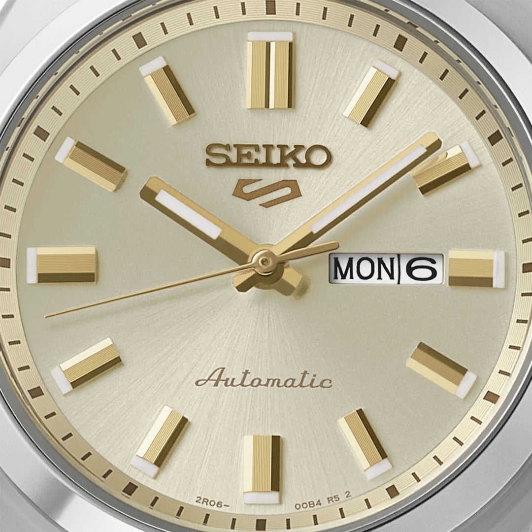 Seiko 5 Sports SRE023K1 dial close-up — cream champagne sunray finish, gold baton hour markers, gold dauphine hands, and day-date display at 3 o&