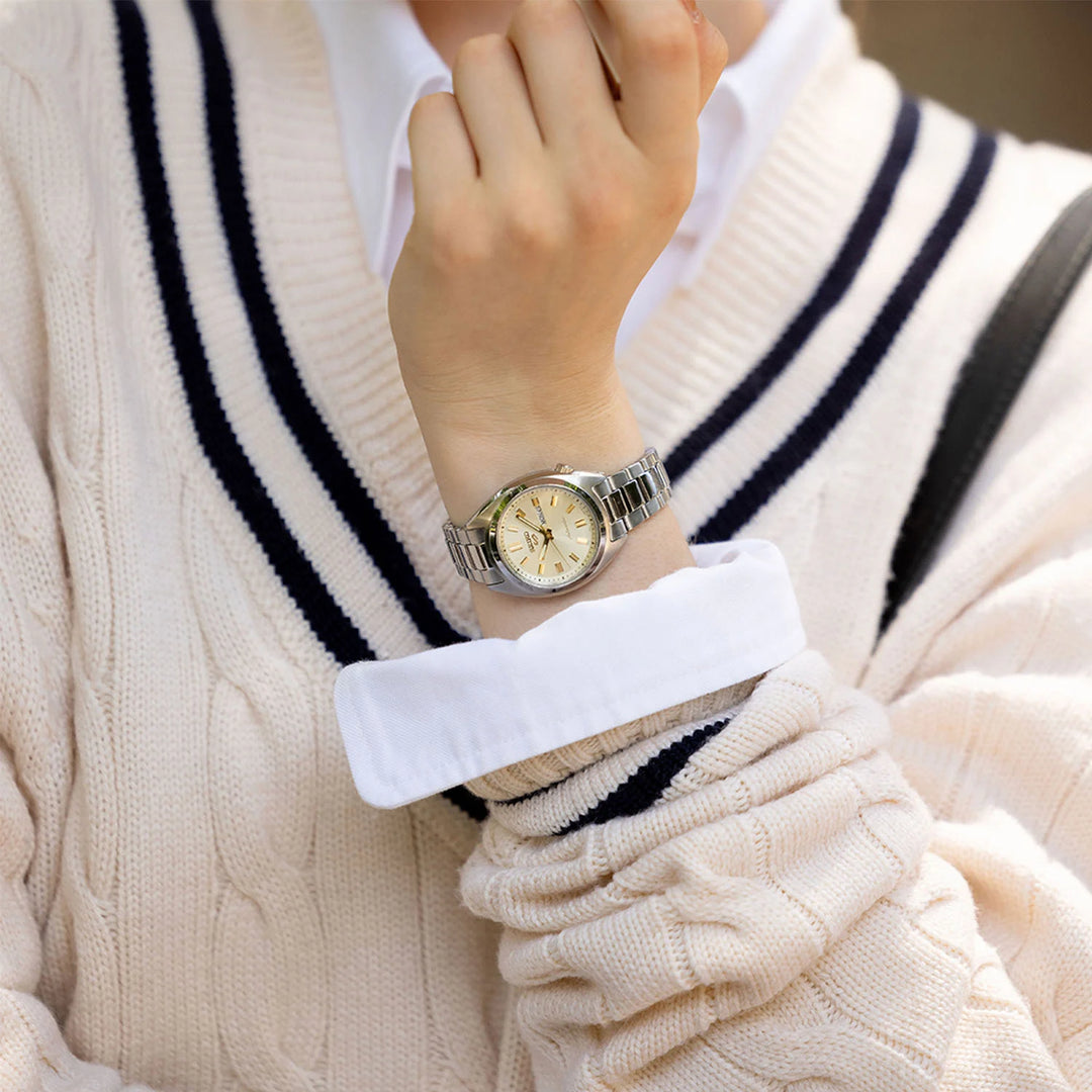Seiko 5 Sports SRE023K1 cream champagne dial watch on wrist, paired with a beige striped knit sweater and neutral trousers