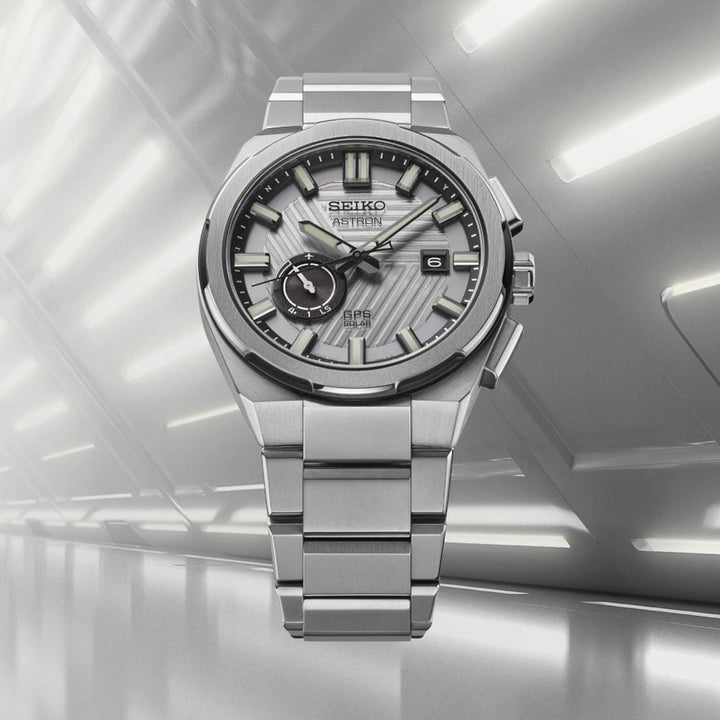 Seiko Astron SSJ037J1 GPS Solar 2025 Limited Edition watch displayed against a silver architectural corridor, highlighting the brushed stainless steel case and textured dial