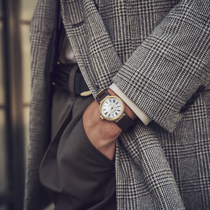 Seiko Presage SPB538J1 145th Anniversary automatic watch worn on wrist — white hand-enamelled dial with Roman numerals, gold-coloured millegrain case, dark brown leather strap, grey check jacket