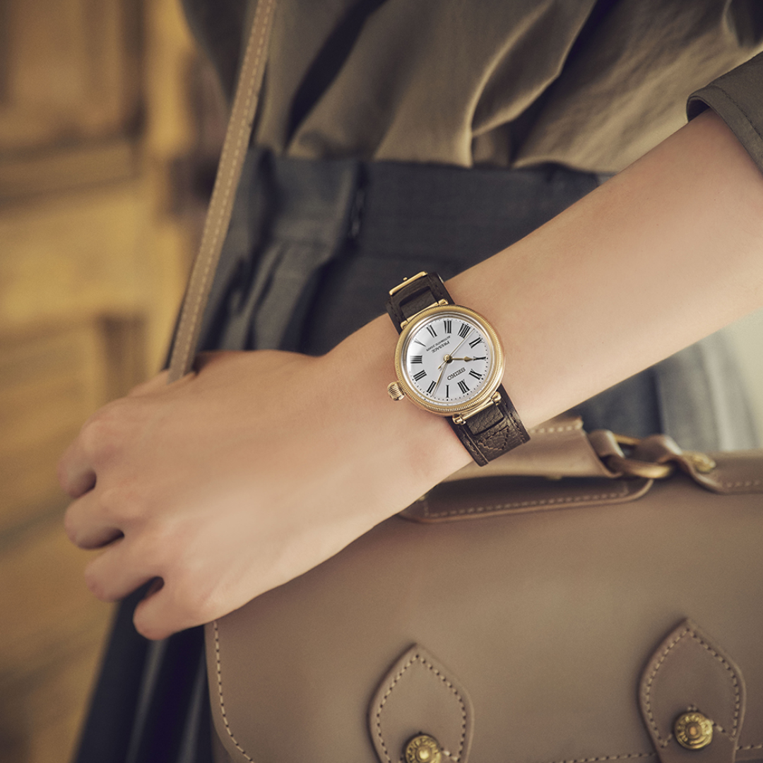 Seiko Presage SPB538J1 145th Anniversary automatic watch worn on wrist — white enamel dial with Roman numerals, gold-tone millegrain case and onion crown, dark brown leather strap