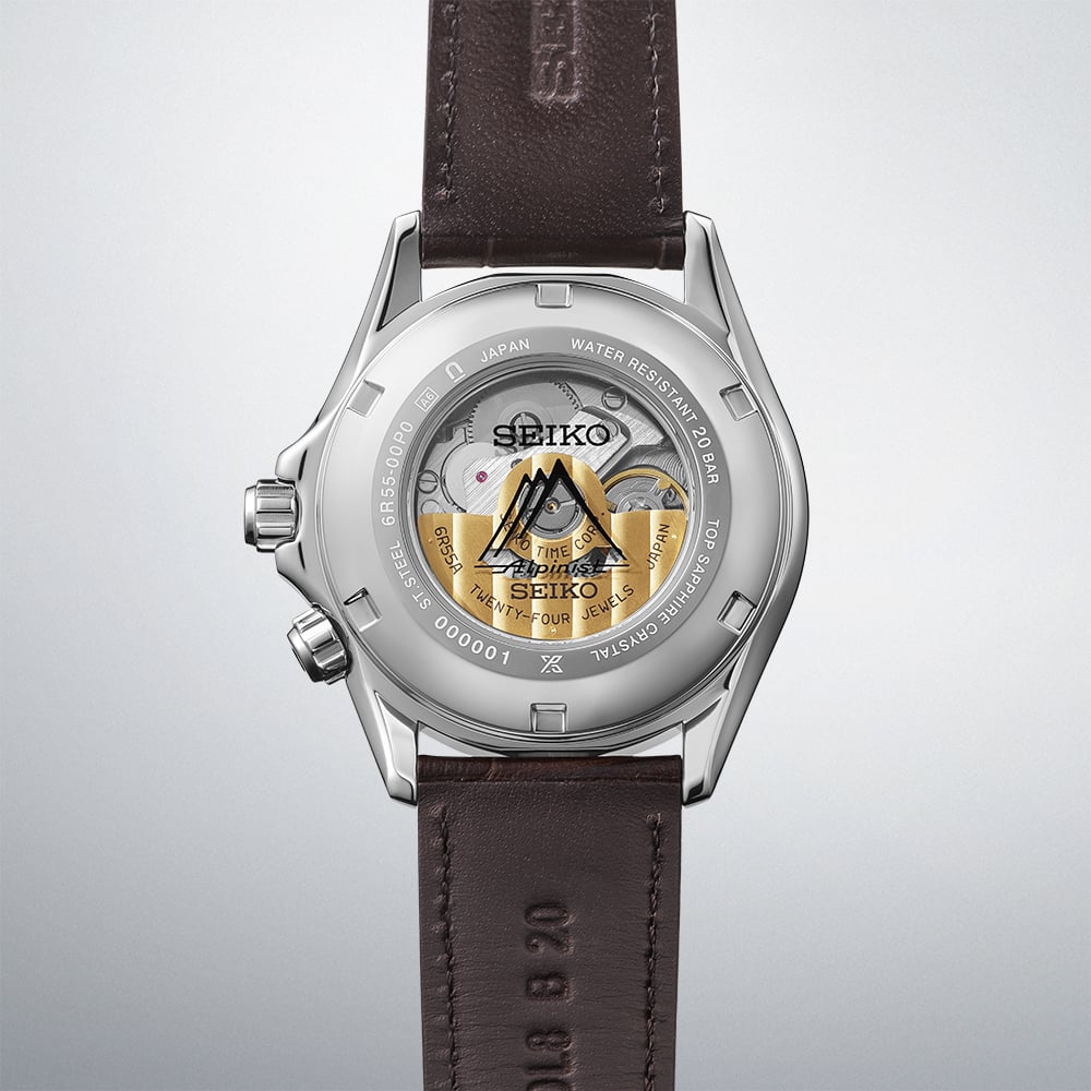 Seiko Prospex Alpinist SPB507J1 open caseback revealing the 6R55 automatic movement with gold Alpinist mountain rotor motif, serial number engraving, and dark brown cow leather strap on gradient grey background